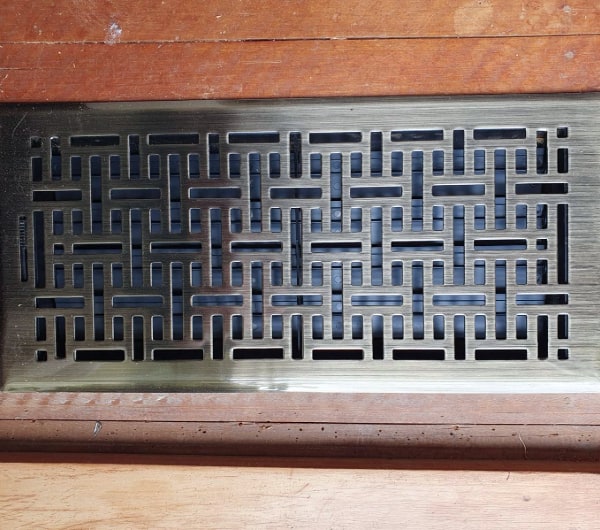 A cast metal floor grille set into a timber floor, the visible part of a ducted heating system in a Dunedin home