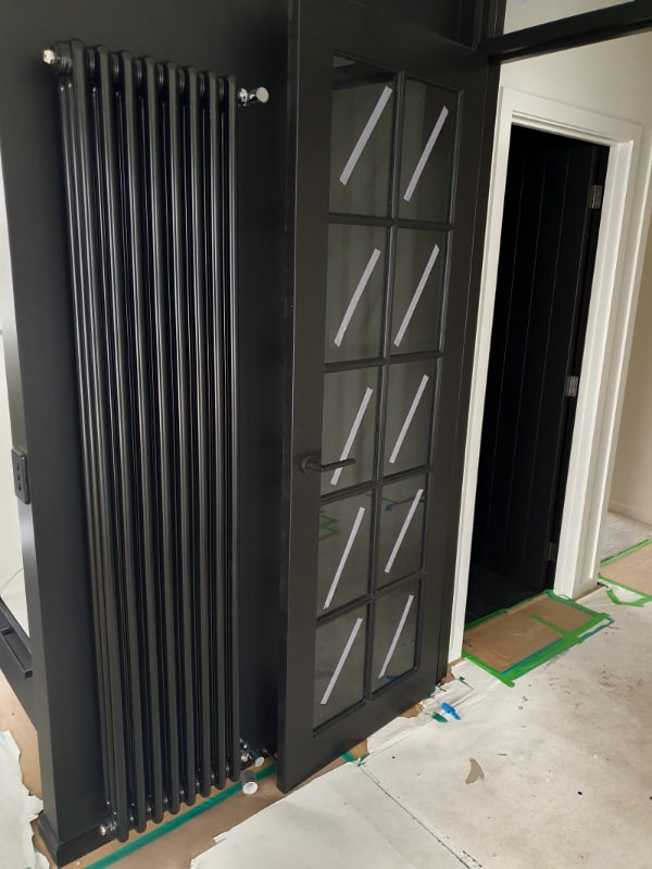 A vertical column radiator in a powder-coated finish, installed beside a glazed door in an Otago home