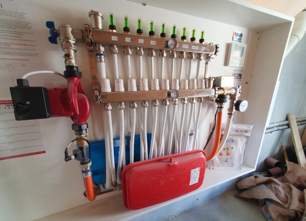 An underfloor heating manifold with circulating pump and zone actuators in an Otago home